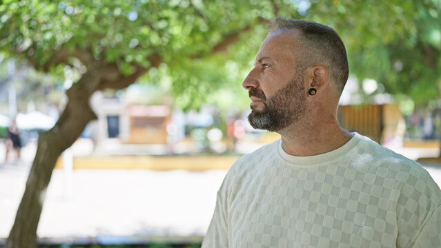 Attractive young man, seriously concentrating while gazing to the side in a sunny, relaxed park setting, embodying a cool, casual lifestyle in the heart of green outdoors