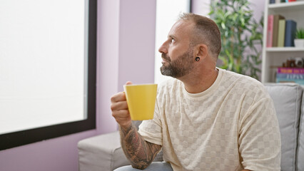 Handsome young man in deep thought, sitting comfortably at home, sipping coffee on a relaxing morning.