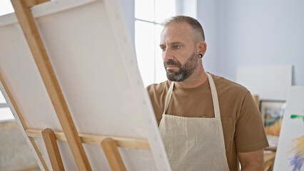 Fototapeta premium Handsome young man artist intensely drawing at his relaxed art studio, a creativity class bursting with paintbrushes, canvas and concentrated adult students.