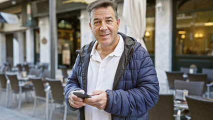 Mature man using smartphone on city terrace captures everyday urban lifestyle and connectivity.