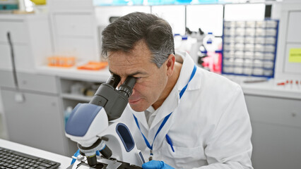 Mature scientist man in lab examining samples with microscope in a modern laboratory indoor setting