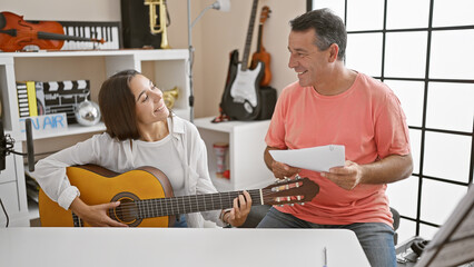 Smiling male and female musicians engrossed in a classic guitar lesson at a cozy music studio,...