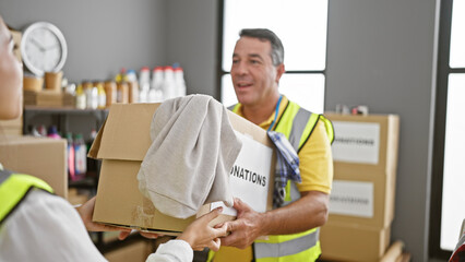 Cheerful man and woman volunteers confidently giving cardboard box full of clothes donation at...