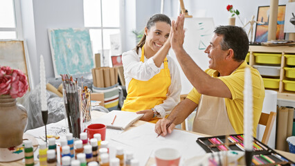 Hispanic man and woman artists high five in joy at art studio while drawing on notebook; vibrant...