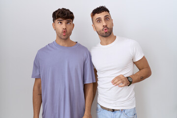 Homosexual gay couple standing over white background making fish face with lips, crazy and comical gesture. funny expression.