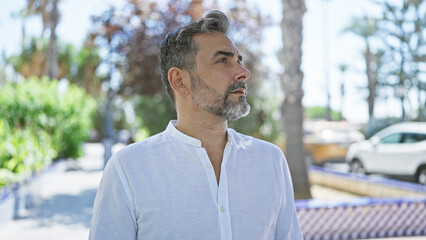 Young hispanic grey-haired man looking to the sky with serious face at park