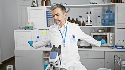 Fototapeta na wymiar Handsome young hispanic grey-haired man, a diligent scientist stretching tired arms after long hours of intense medical research in the lab
