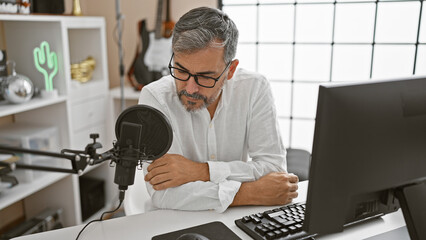Grey-haired, young hispanic man on-air at radio studio, a serious news reporter with a beard,...