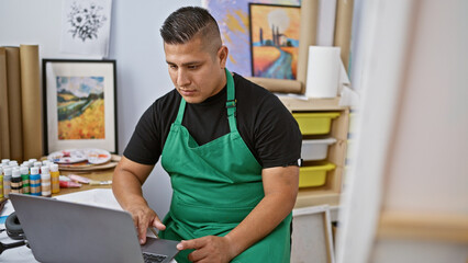 Fototapeta premium Handsome latin artist, a young man, immersed in his craft, masterfully painting with his laptop in a vibrant art studio