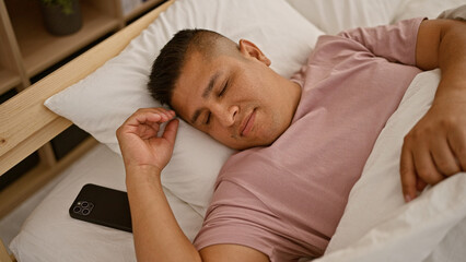 Young, handsome latin man, relaxing comfortably in his cozy bedroom, lying on sleep-retaining bed,...