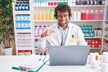 Hispanic young man working at pharmacy drugstore working with laptop pointing finger to one self...