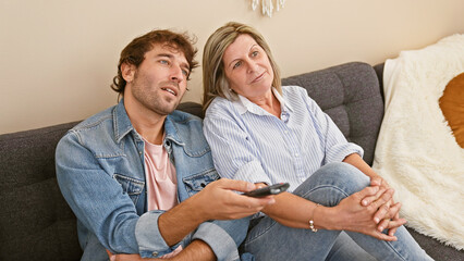 Mother and son restfully immersed in a movie at home, comfortably sitting together on the sofa,...