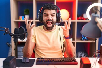 Hispanic man with beard playing video games with headphones celebrating mad and crazy for success...