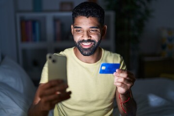 Young arab man using laptop and credit card sitting on bed at bedroom