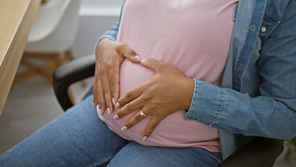 Fototapeta premium Heartwarming moment, young successful pregnant businesswoman at office, forming a heart gesture with her hands over belly, embracing upcoming motherhood indoors