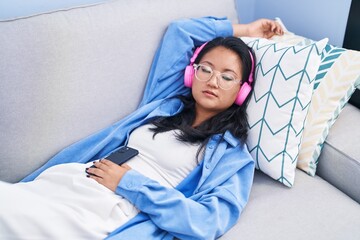 Young chinese woman listening to music sleeping on sofa at home