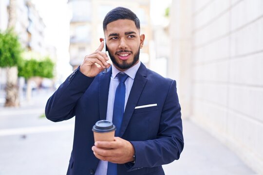 Young latin man business worker talking on smartphone drinking coffee at street