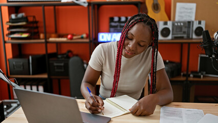 Smiling african american woman musician masterfully taking notes on laptop during exciting video...