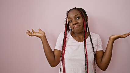 Clueless african american woman with braids, standing unsure over a pink isolated background,...