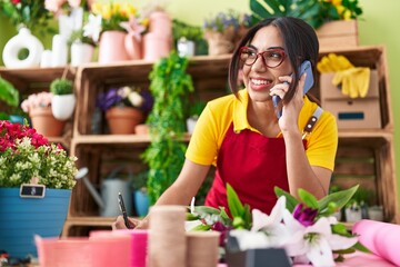Young beautiful arab woman florist talking on smartphone writing on notebook at flower shop