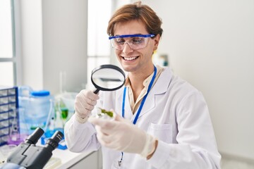 Young caucasian man scientist looking plant sample with loupe at laboratory