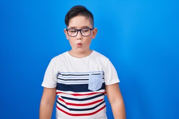 Young hispanic kid standing over blue background making fish face with lips, crazy and comical gesture. funny expression.