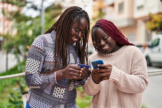 African american women friends using smartphone and credit card at street