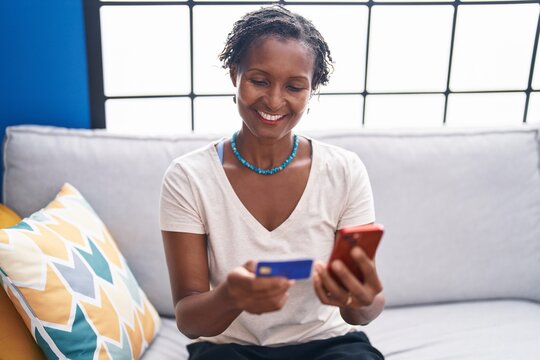 Middle age african american woman using smartphone and credit card sitting on sofa at home