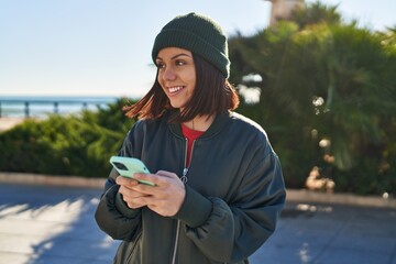 Young beautiful hispanic woman smiling confident using smartphone at seaside