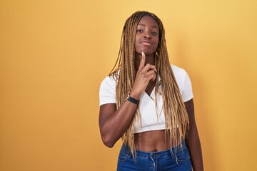 African american woman with braided hair standing over yellow background thinking concentrated...