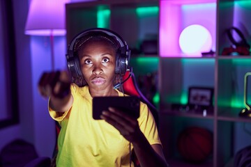 African american woman playing video games with smartphone pointing with finger to the camera and to you, confident gesture looking serious