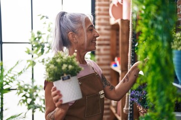 Middle age grey-haired woman florist holding plant pot at florist