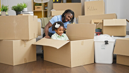 African american father and daughter playing with cardboard box as a car at new home
