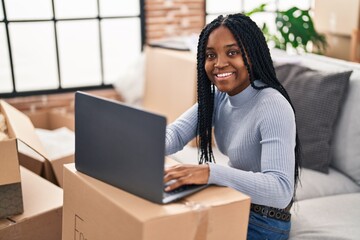African american woman using laptop sitting on sofa at new home