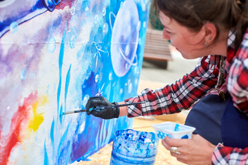 Naklejka premium Female painter draws picture with paintbrush on canvas for outdoor street exhibition, close up side view of female artist apply brushstrokes to canvas, symphony of art creativity