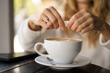 Girl in a cafe. Young woman adding sugar to delicious coffee at table