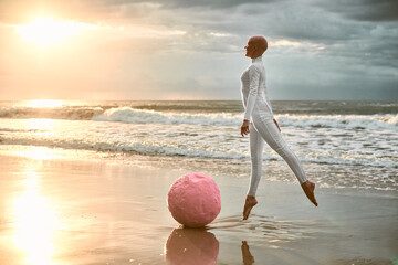 Hairless ballerina with alopecia in white futuristic suit jumps next to pink sphere and soaring...