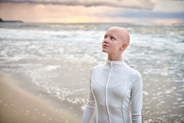 Close up portrait of young hairless girl with alopecia in white futuristic costume on sea...