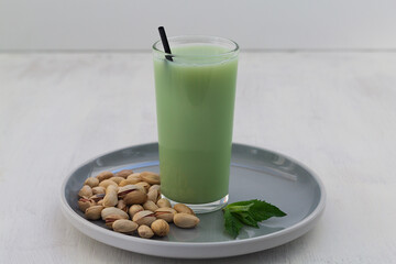 smoothie with nuts. Alternative milk. glass of Natural plant based Pistachio milk with pistachionuts and green mint on the white table. A paper straw in a glass. Healthy diet. copy space