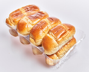 Close-up of fresh, golden-brown dinner rolls in a plastic tray against a white background.