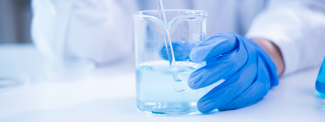 Closeup scientist hand using stirring rod for stirring blue liquid solution glass beaker chemical chemistry research science experiment test laboratory, scientific medicine technology lab analysis