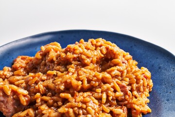 Close-up of homemade risotto with sausage on a blue plate against a white background, highlighting textures and colors.