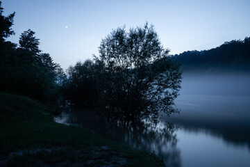 Misty mountain river with forest on the banks at night.