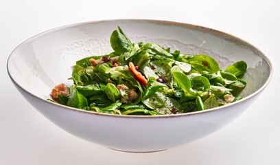 Fresh spinach salad with bacon, walnuts, and vinaigrette in a white bowl on a clean background.