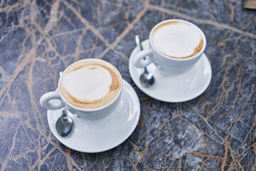 Two cappuccinos with frothy cream on a marbled table, symbolizing a casual meeting or a coffee break.