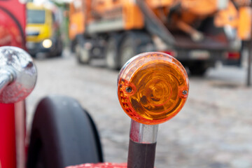 
An orange car lamp on a red car wing on the background of a heavy machine