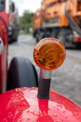 
An orange car lamp on a red car wing on the background of a heavy machine