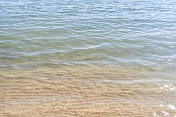 Clear waters gently lap the sandy shores of a tranquil beach, absent of any people.
