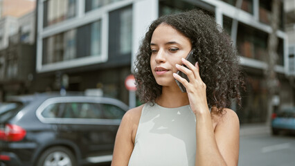 Young beautiful hispanic woman talking on smartphone with serious expression at street