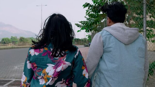 Rear view of a young couple walking together in a park sidewalk symbolizing togetherness and casual lifestyle